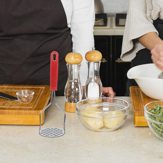 Kitchen counter with cooking utensils and ingredients, including a masher, bowls, and pepper grinders.