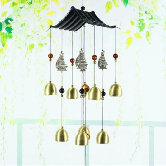Decorative wind chime with gold bells and black roof design against a light green background